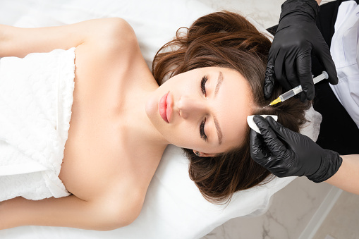 Mesotherapy,  vitamin injections in head skin of hair area. Professional hair loss treatment. Close up view of woman head and doctor's hands with syringe. View above.
