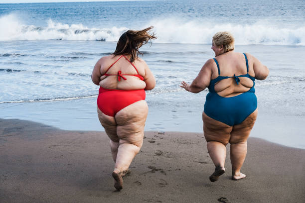 plus-size-freunde, die während der sommerferien am strand spazieren gehen und spaß haben - konzentrieren sie sich auf mädchen zurück - child obesity stock-fotos und bilder