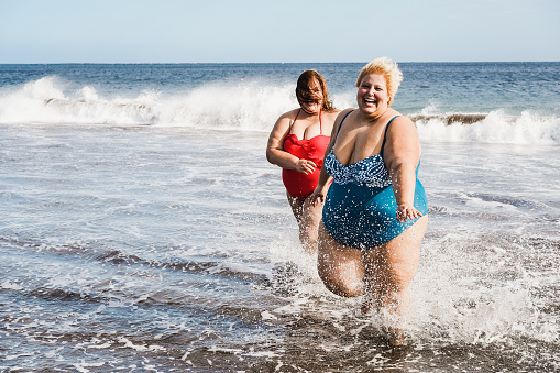 Plus size friends walking on the beach having fun during summer vacation - Focus on right girl face