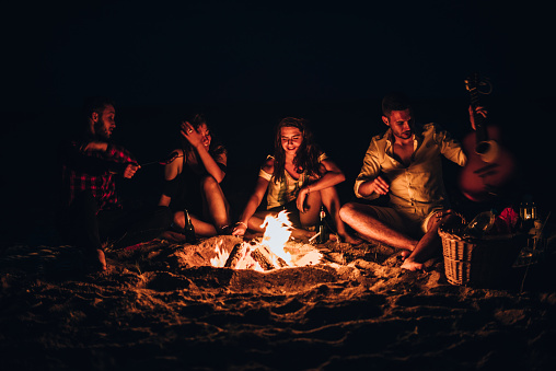 Happy friends playing music and enjoying bonfire in nature