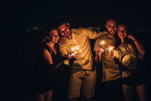istock Group of people is holding sparkle sticks while enjoying on the beach by night 1385106336