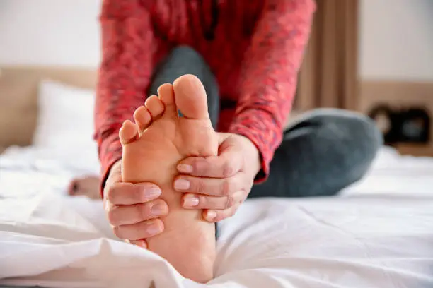 Female massaging bare foot in bed, close up. Stretching leg  muscles in the morning and doing foot acupressure