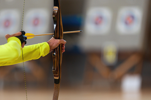Archer holds his bow aiming at a target, archery as a sport discipline in the hall. Competition for the best shot an arrow into targets