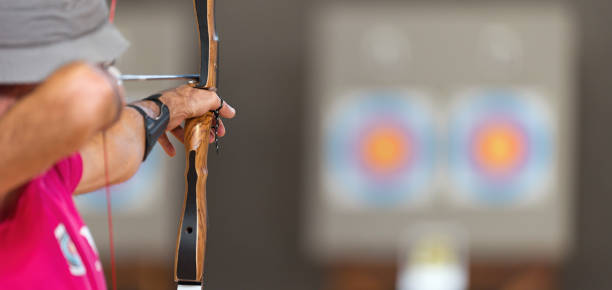 Archer holds his bow aiming at a target, archery as a sport discipline in the hall. Competition for the best shot an arrow into targets