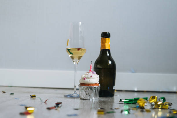 bottiglia e bicchiere di champagne e cupcake con candela sul pavimento con coriandoli dopo la festa di compleanno a casa - solitude loneliness bedroom empty foto e immagini stock