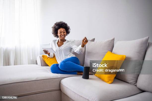 Black Woman Connecting Phone To Her Virtual Assistant Smart Speaker Stock Photo - Download Image Now