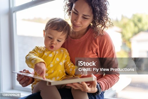 istock Affectionate mother reading book with adorable toddler daughter 1385109628