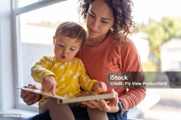Affectionate Mother Reading Book With Adorable Toddler Daughter Stock Photo - Download Image Now
