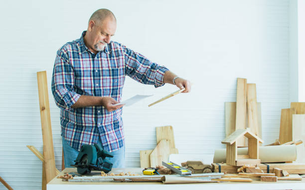 istock Senior Caucasian retired old male woodworker, carpenter reading, rechecking and comparing drawing plan with finish wooden figure toy or furniture before giving to customer. Hobby, Retirement Concept. 1385109685