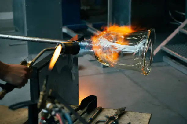 Close up of a glassblower artisan shaping the hot molten glass at strong fire inside a workshop. Manual glass processing by the craftsmen inside a glass factory