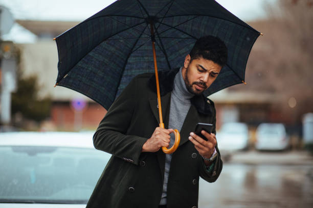istock Young businessman using smart phone under umbrella 1385112223