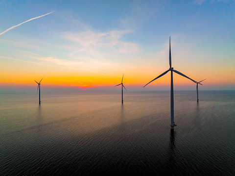 Wind turbines producing sustainable renewable energy in an offshore wind park in Flevoland, The Netehrlands, during sunset. Drone point of view.