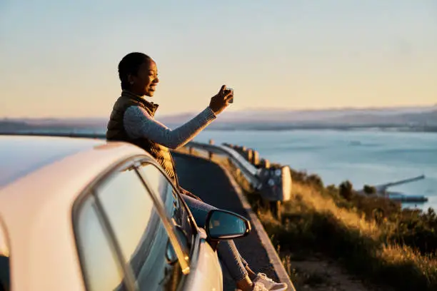 Photo of Shot of a young woman taking pictures of the view on a road trip