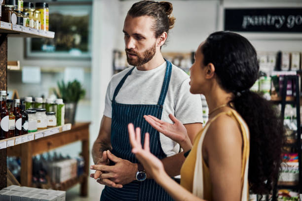Shot of a young man helping a customer while she shops in his organic store stock photo
