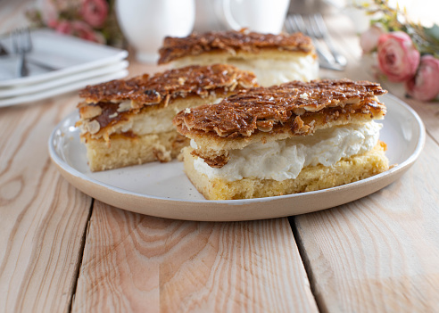 Delicious homemade baked sheet cake with whipped cream filling and caramelized almond topping. Served on a plate on wooden table. Ready to eat.