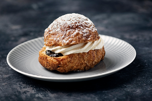 Semla or Fastelavnsbolle or Fastelavn cakes are a Danish delicacy made and eaten in great quantities in many parts of Scandinavia  in the period up to the beginning of Lent. Made from puff pastry and filled with cream and or jam and topped with a variety of different flavour. Here it has been filled  with prune jam, whipped cream and topped with powdered sugar. Colour, horizontal format with some copy space.