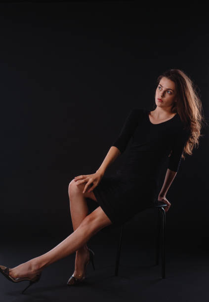 Body shot of  a provocative modern girl wearing black skirt and black high heels sitting on chair