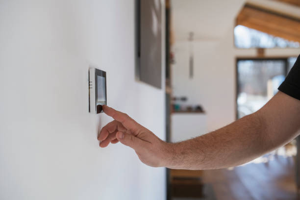 hombre en casa ajustando termostato con dispositivo en la pared. - termostato fotografías e imágenes de stock