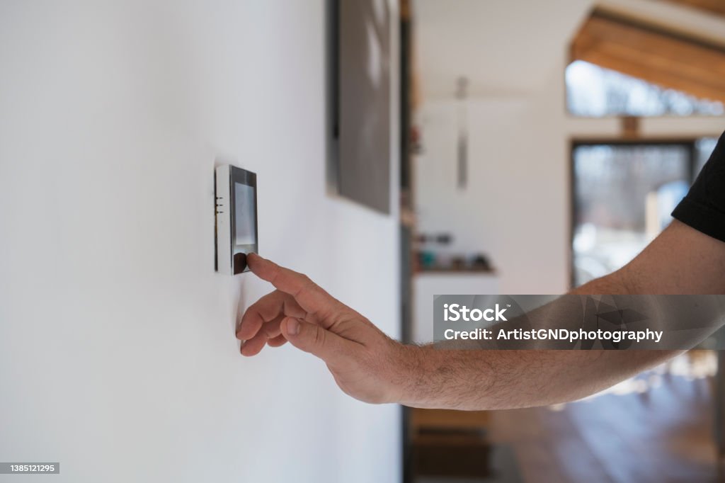 Man at home adjusting thermostat with device on the wall. Unrecognisable man at home adjusting thermostat with device on the wall. Thermostat Stock Photo