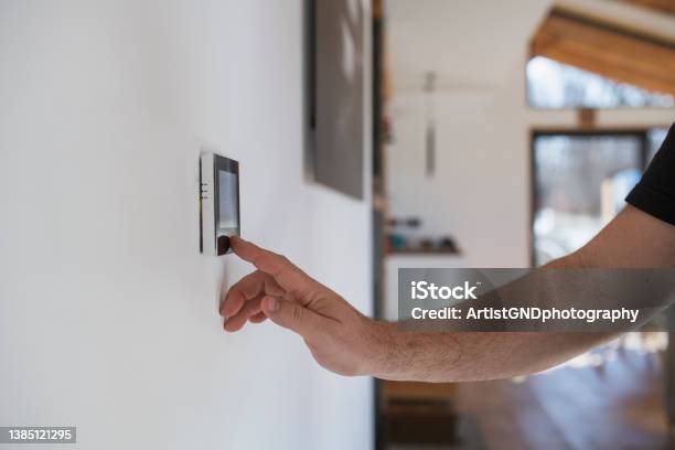 Man At Home Adjusting Thermostat With Device On The Wall Stock Photo - Download Image Now