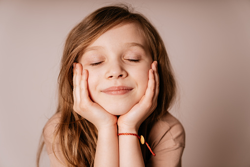 Cute Six year old girl smiling and holding her face with her hands with eyes closed.