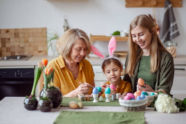 frohe ostern familie ältere großmutter und junge frau mutter blond mit kleiner tochter mit hasenohren bereiten sich auf den urlaub vor, um eier zu malen - easter easter bunny fun humor stock-fotos und bilder