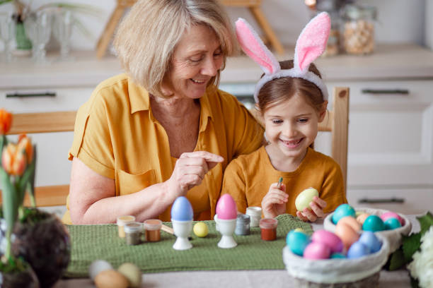 frohe ostern familie ältere großmutter und kleine enkelin mit hasenohren bereiten sich auf den feiertag vor, um eier zu malen - easter easter bunny fun humor stock-fotos und bilder