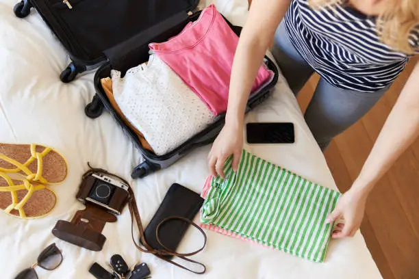 A young woman with blond long hair packs her clothes for a city trip in her suitcase in her bedroom, high res with copy space