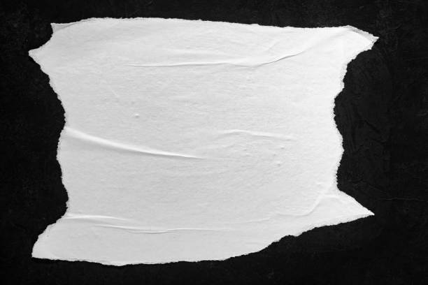 istock Sheet of white paper with torn edges on a black wall. 1385141263