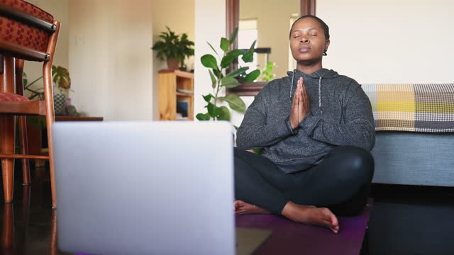 Young woman meditating at home during an online yoga class on a laptop