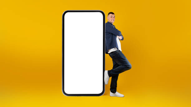 istock Guy Leaning On Big Smartphone With Blank Screen, Yellow Background 1385150763