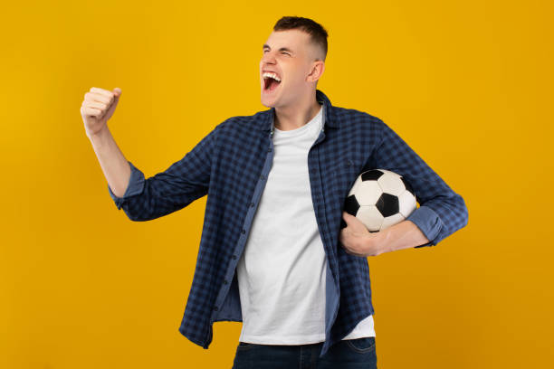 istock Man Shouting Gesturing Yes Holding Ball Celebrating Victory, Yellow Background 1385153799