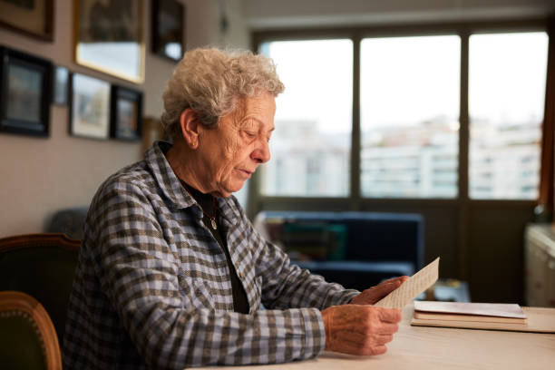 istock Old woman reading a letter at home. 1385154070