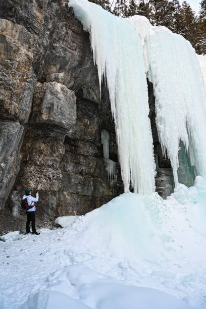 istock Female hiker relaxes under frozen waterfall 1385155672