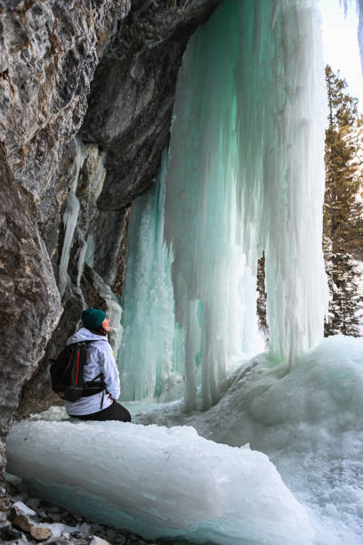 istock Female hiker relaxes under frozen waterfall 1385155684