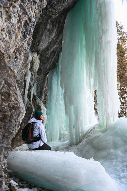 istock Female hiker relaxes under frozen waterfall 1385155732