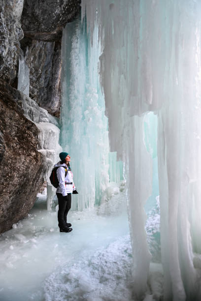 Female hiker relaxes under frozen waterfall