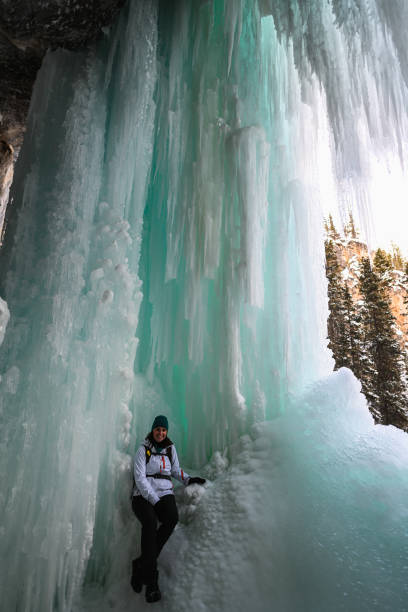 istock Female hiker relaxes under frozen waterfall 1385155823