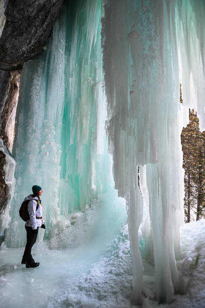 istock Female hiker relaxes under frozen waterfall 1385155824