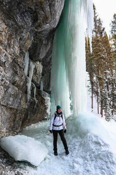 istock Female hiker relaxes under frozen waterfall 1385155886