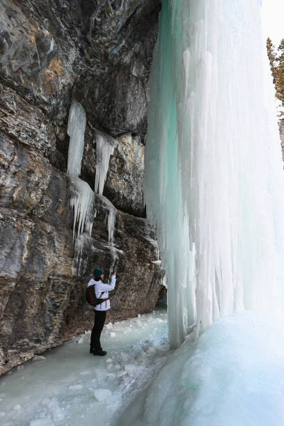 istock Female hiker relaxes under frozen waterfall 1385155887