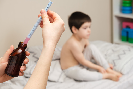 The pediatrician or mother types in a measuring syringe the medicine for cough or temperature syrup for the child.
