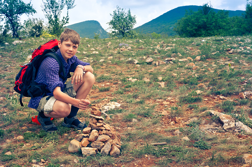 Young tourist with backpack collects pyramid from the stones on top of the mountain. Crimea