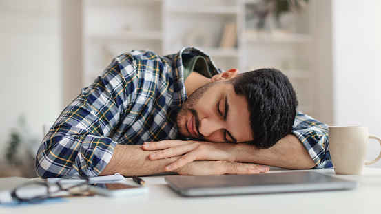Exhausted Young Man Sleeping At Work Sitting At Desk
