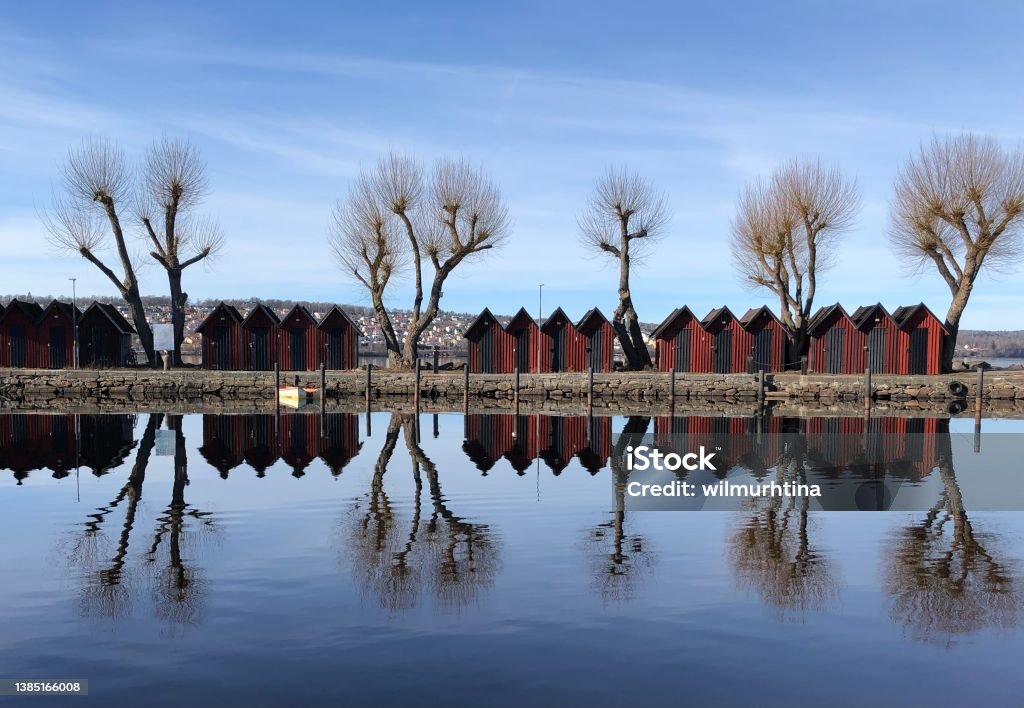 Red boat houses in the harbor of Jönköping;  Lake Vättern, Jönköping, Sweden. Beautiful reflexions in the water. A sunny day in march with clear blue sky. Bare trees reflecting in the calm water. Lake Stock Photo