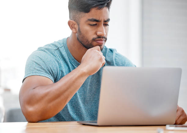 istock Shot of a handsome young man sitting alone at home and looking contemplative while using his laptop 1385170846