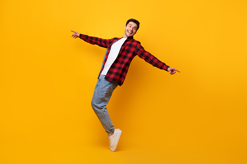 Happy excited funny man dancing to favorite song standing on tiptoes isolated over yellow orange studio background wall, pointing at copy space. Male doing disco moves enjoying sound and music, banner