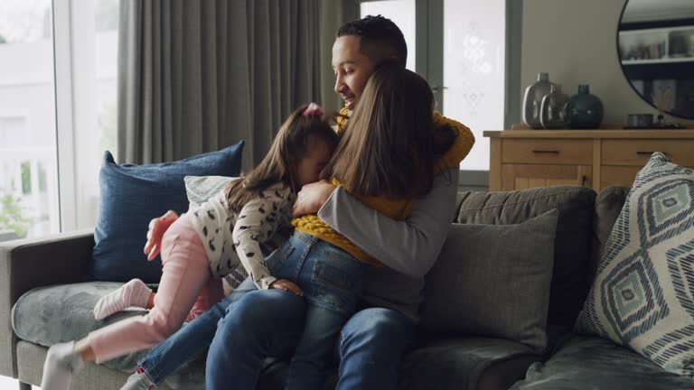 4k video footage of two little girls embracing their father on the sofa at home