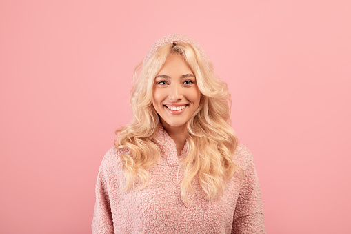 Happy person. Portrait of friendly blonde lady with beautiful smile, wearing hoodie and smiling at camera, posing in studio over pink background, closeup shot with copy space