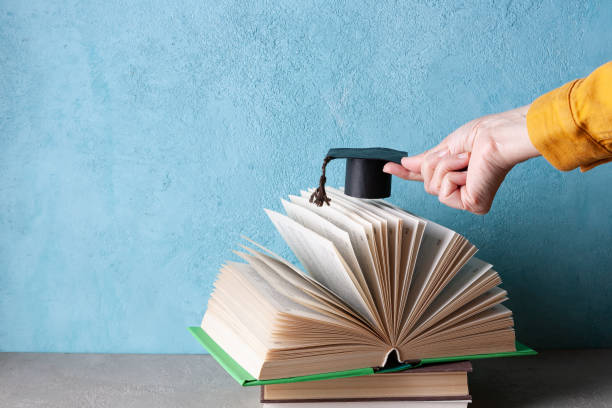istock woman's hand holding a paper student hat over an open book 1385175290